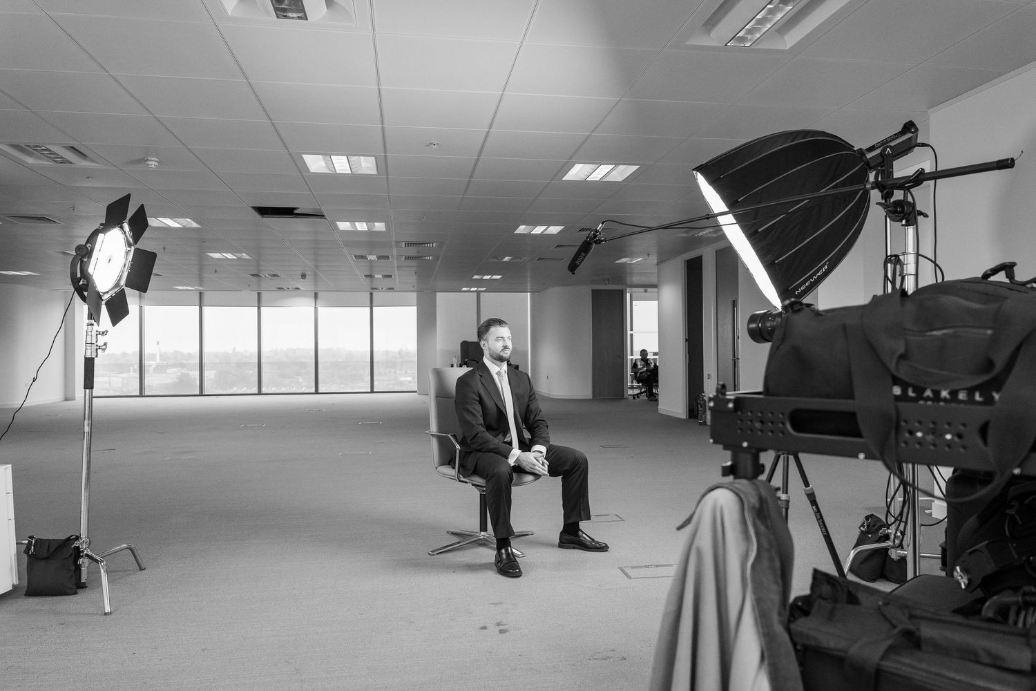 Film crew setting up professional lighting and camera equipment in a modern office space with large windows.