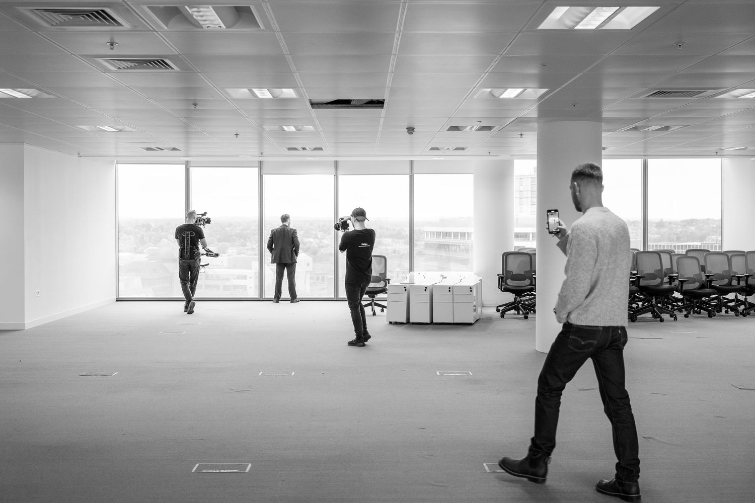 People walking through a bright, empty office space with fluorescent lighting and white walls.