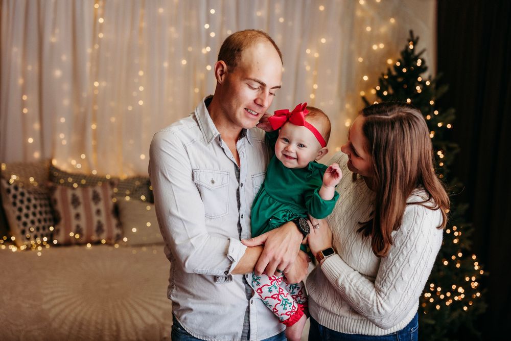 Family enjoying holiday moments together in front of Christmas lights and decorated tree.