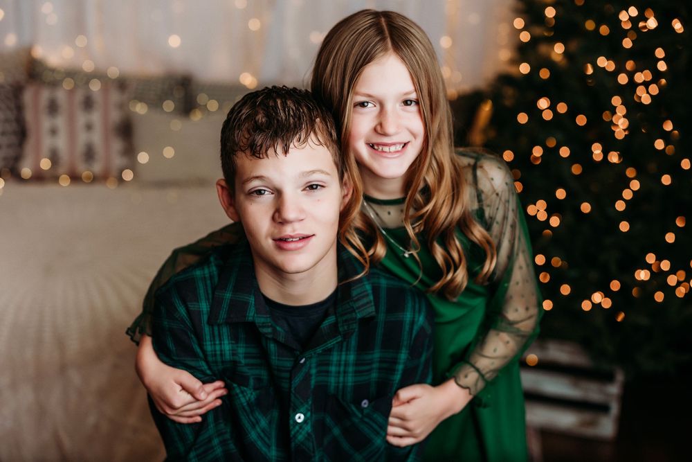 People in green holiday attire pose for photos in front of twinkling Christmas lights and festive decor.