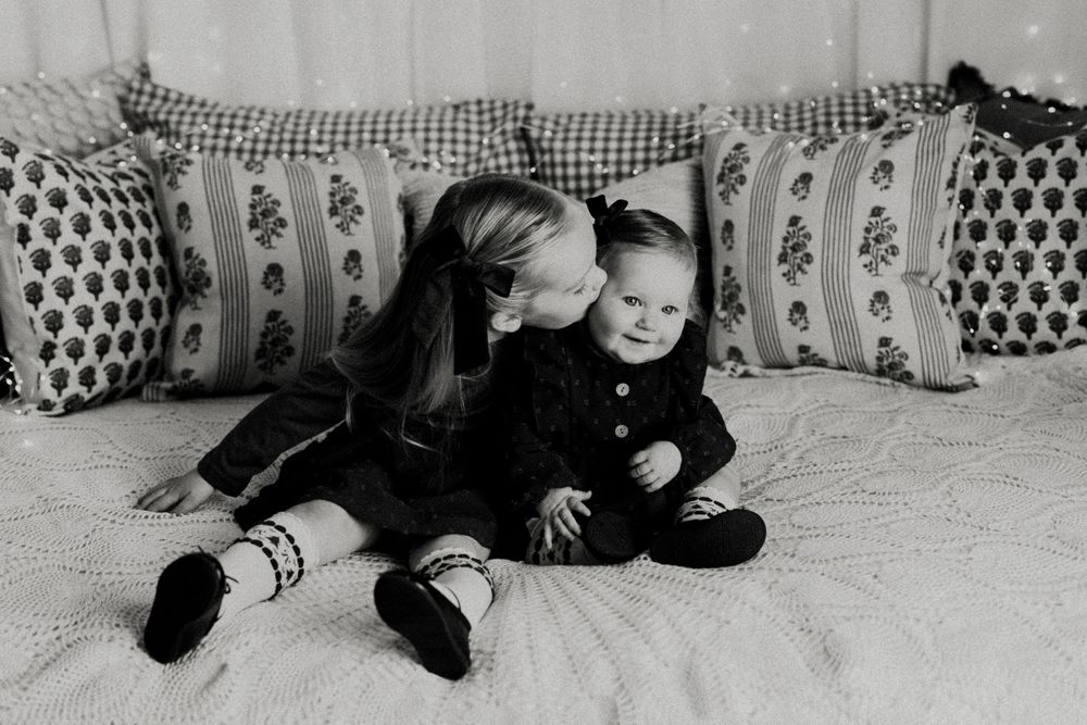 A black and white photograph shows two children sitting together on a couch with decorative throw pillows.