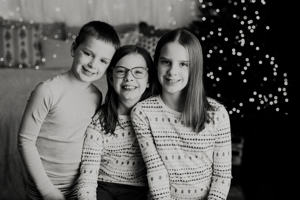 A black and white photo collage showing six similar family portraits with holiday lights in the background.
