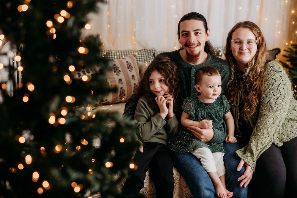 A family shares joyful moments together during a holiday photoshoot with twinkling Christmas lights in the background.