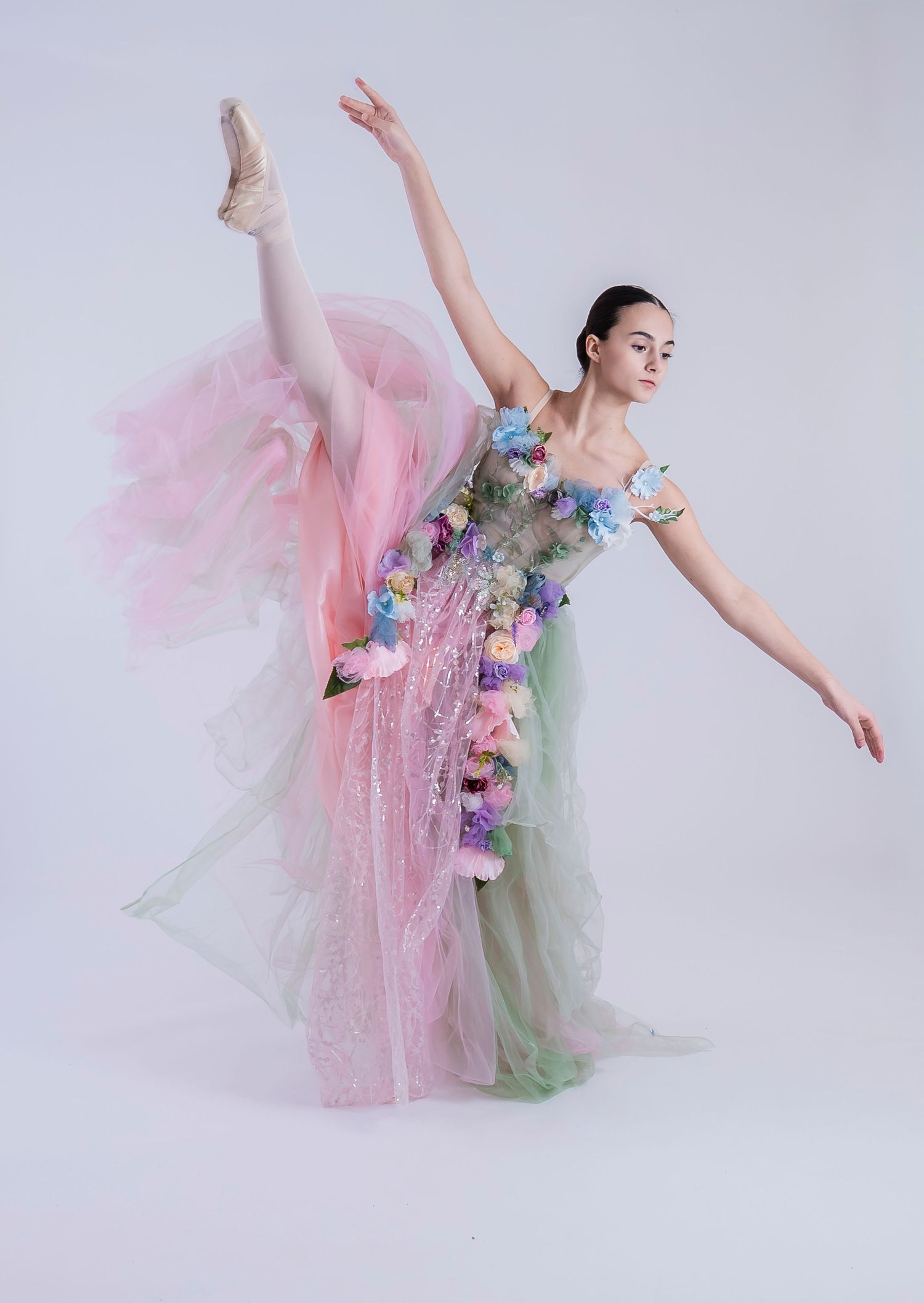 A ballet dancer in a flowing pink and green tulle dress performs graceful poses against a light backdrop.