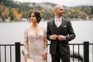A couple poses for wedding photos on a lakeside dock during autumn with mountains and fall foliage in the background.
