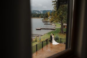 Couple embracing on a scenic lakeside deck with mountains and evergreen trees in the background.