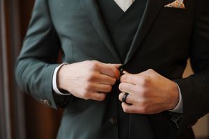 Close-up shot of hands adjusting a black suit jacket button in formal attire.
