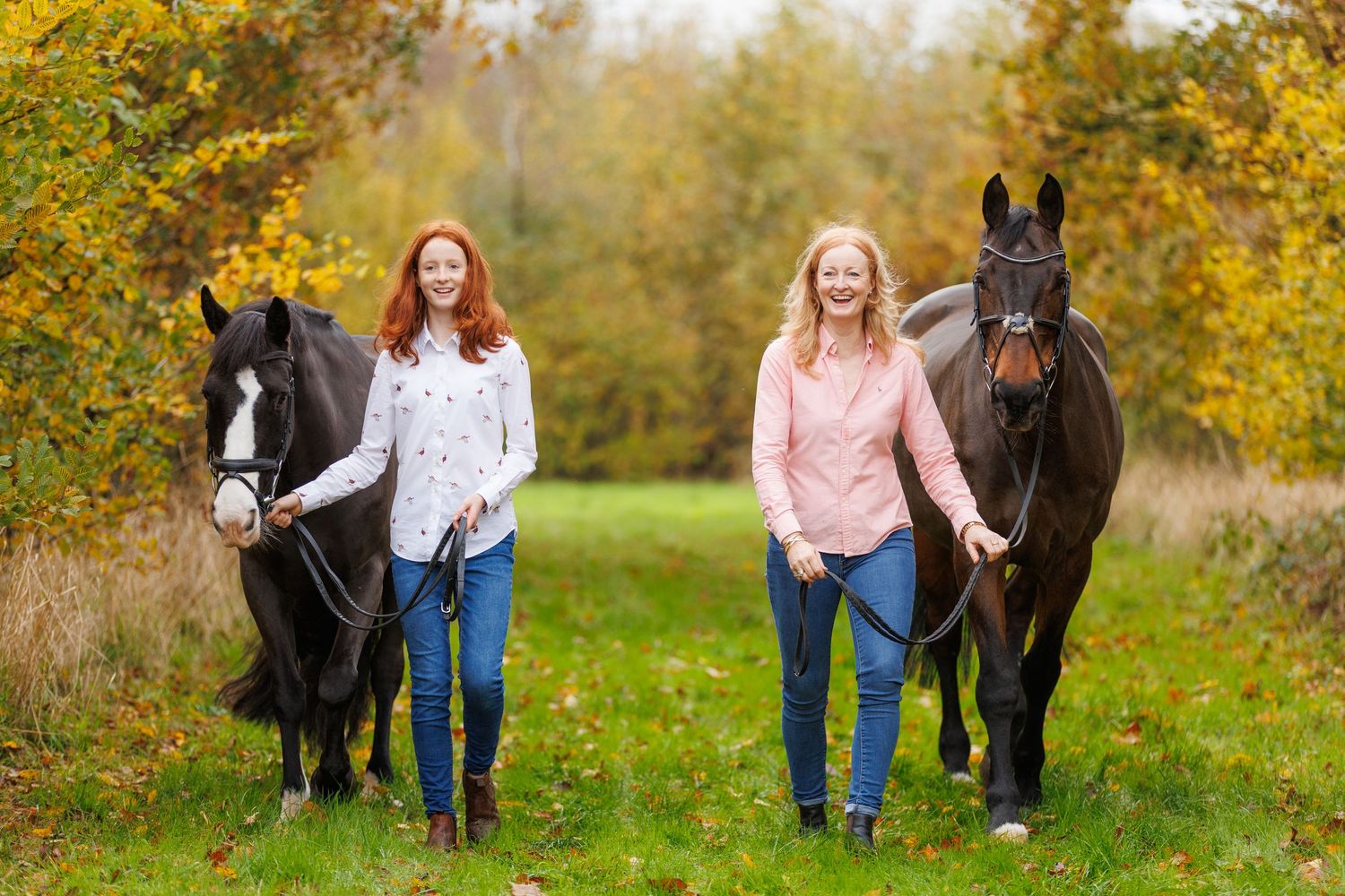 People walking with a black horse through autumn foliage in a scenic outdoor setting.
