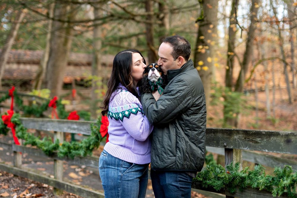 Couple sharing sweet moment with their Cavalier King Charles Spaniel near holiday garland fence.