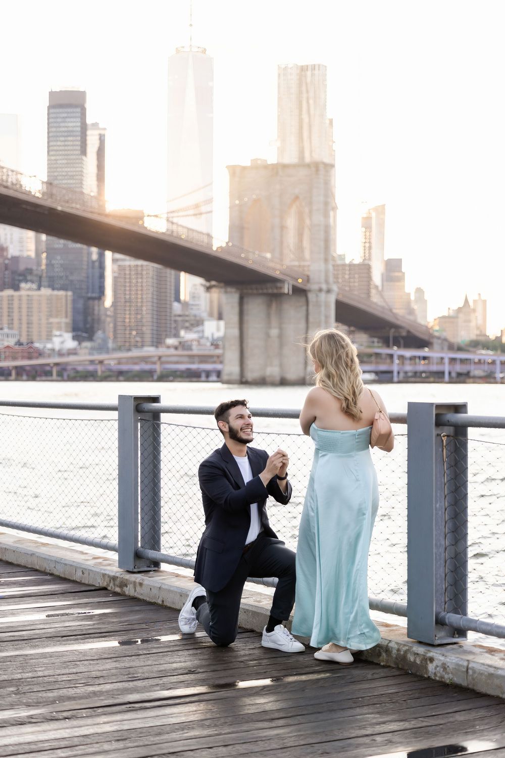 Romantic moment on a wooden pier with city skyline and bridge silhouetted against the bright sky.