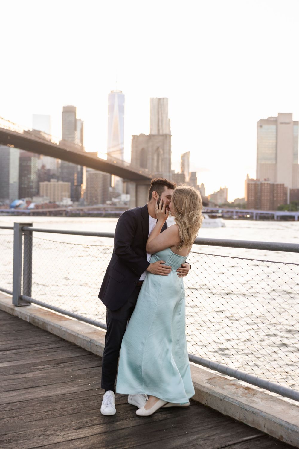 Romantic couple sharing intimate moments on a waterfront pier with city skyline in the background at sunset.