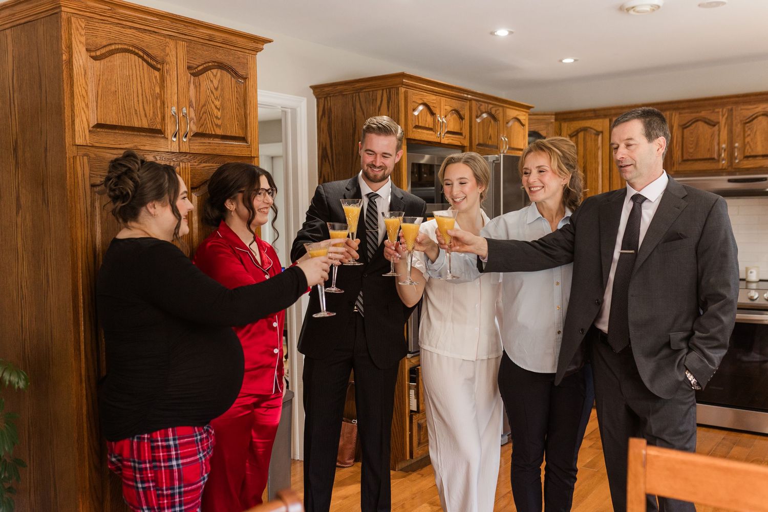 People in formal attire gather in a kitchen for a celebratory toast with champagne glasses.