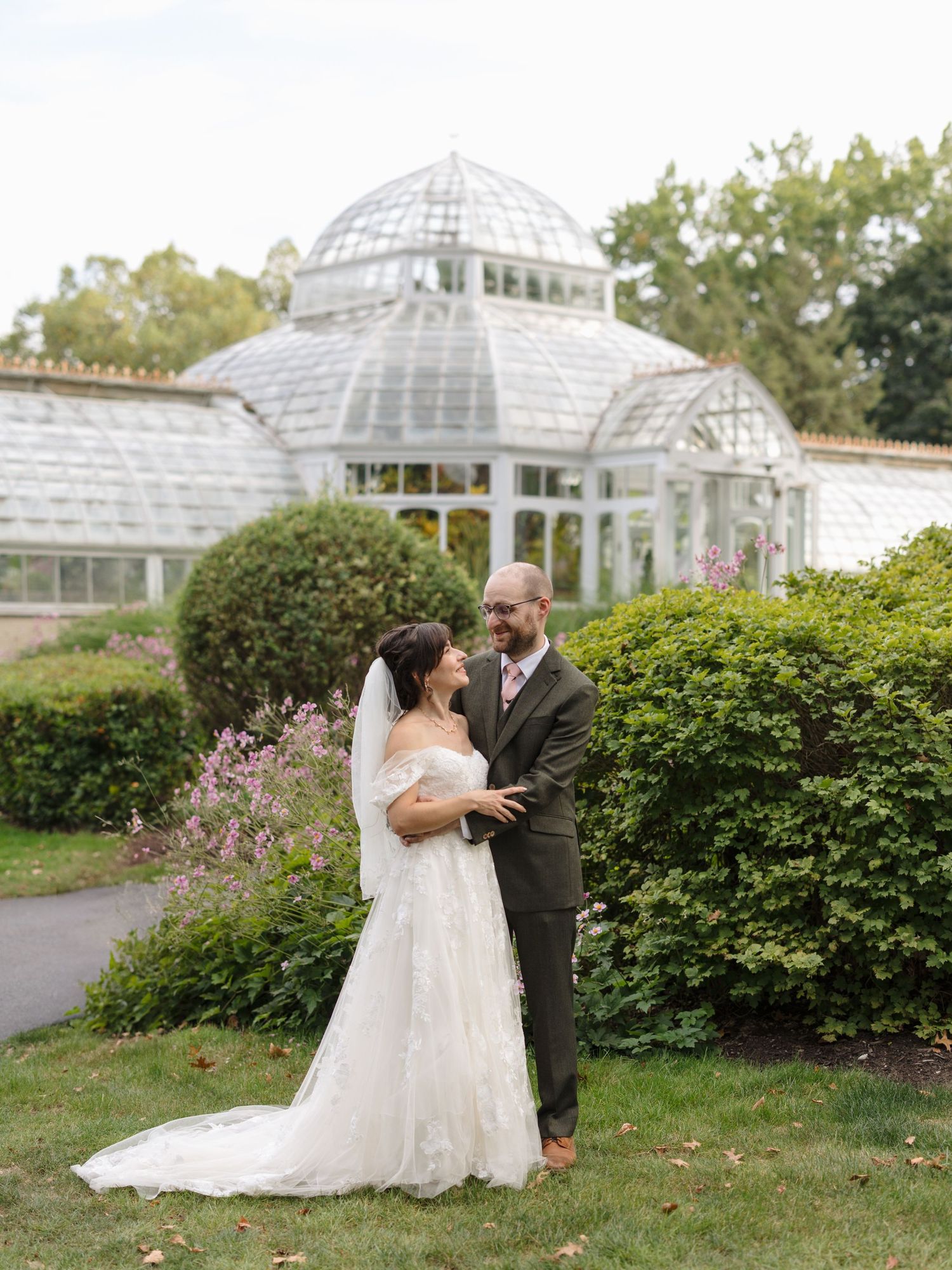 Wedding couple embraces in front of a beautiful greenhouse conservatory with white domed architecture.