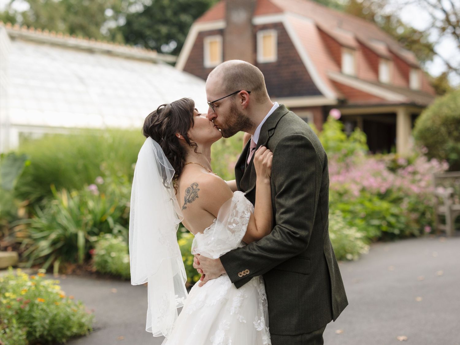 A couple shares a romantic kiss in front of a scenic garden backdrop during their wedding celebration.