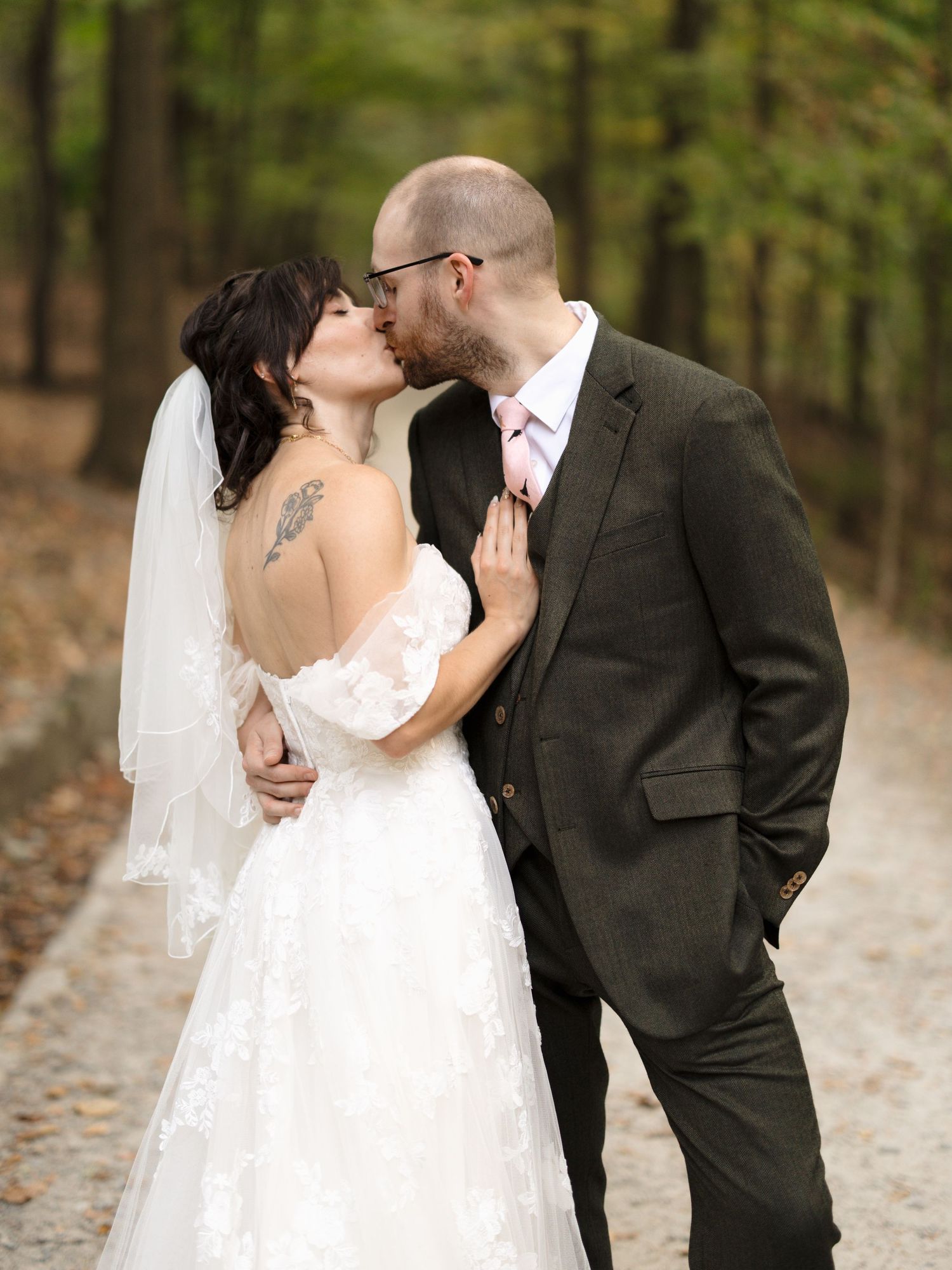 A romantic wedding couple shares an intimate moment on a wooded path covered in fall leaves.