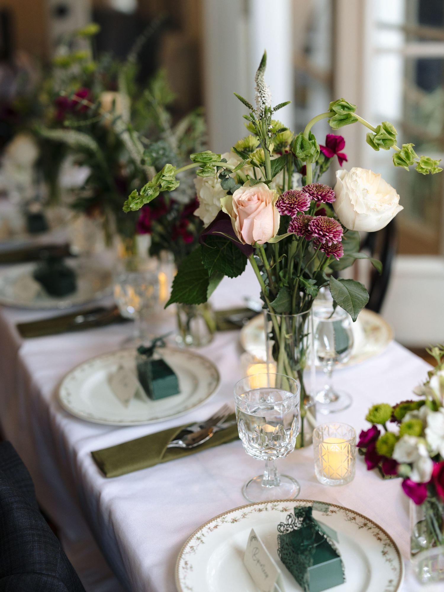 Elegant table setting with pink and burgundy floral centerpiece, white linens, and glowing candles at a formal dinner.