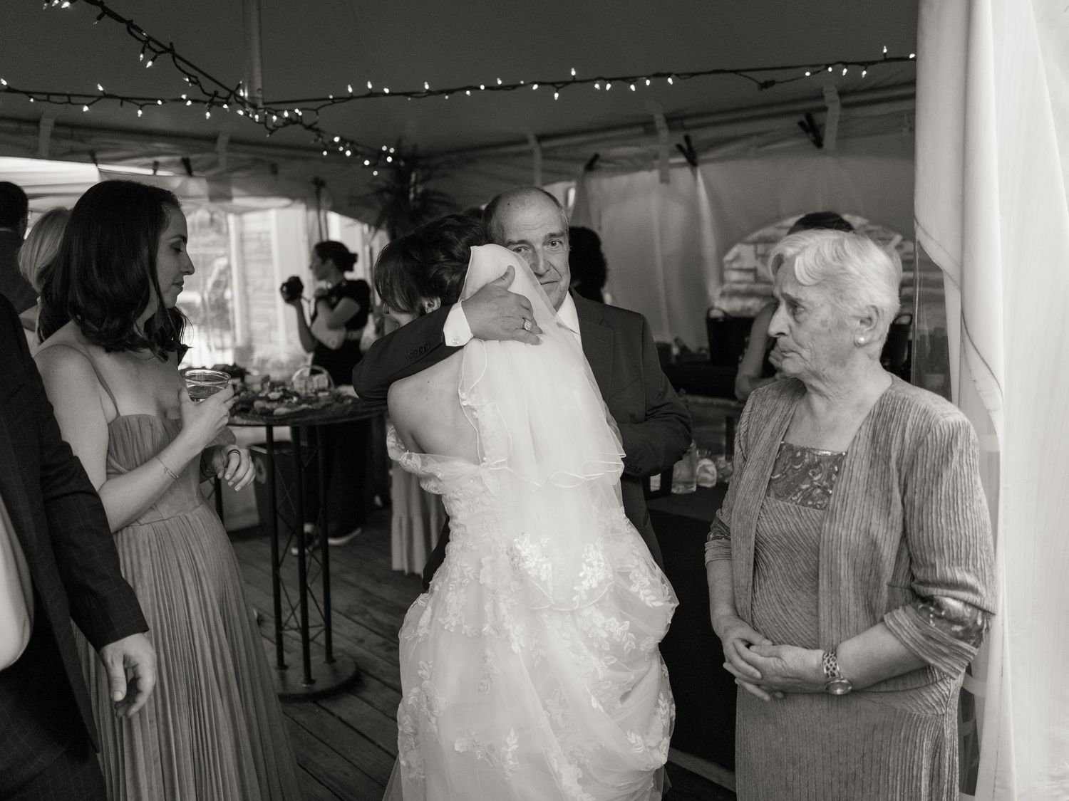 Wedding guests dance and celebrate under string lights at an indoor reception venue.
