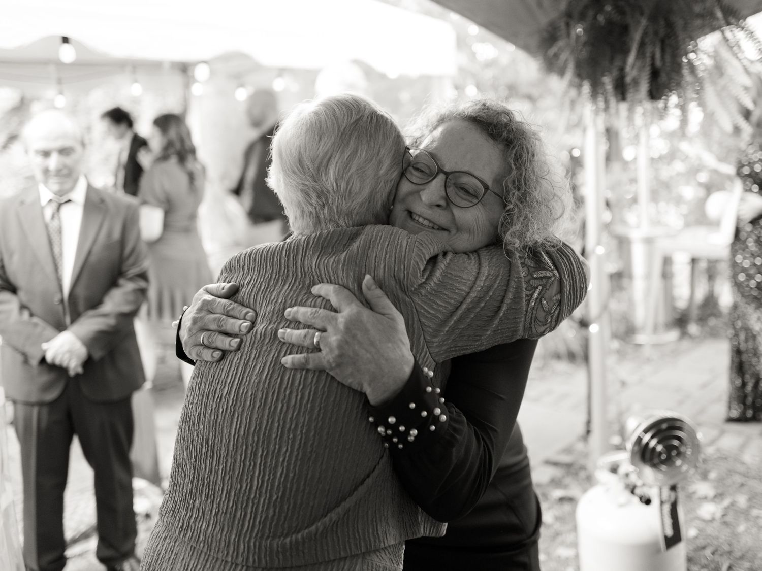 A heartfelt embrace captured in black and white at an outdoor celebration under a tent.