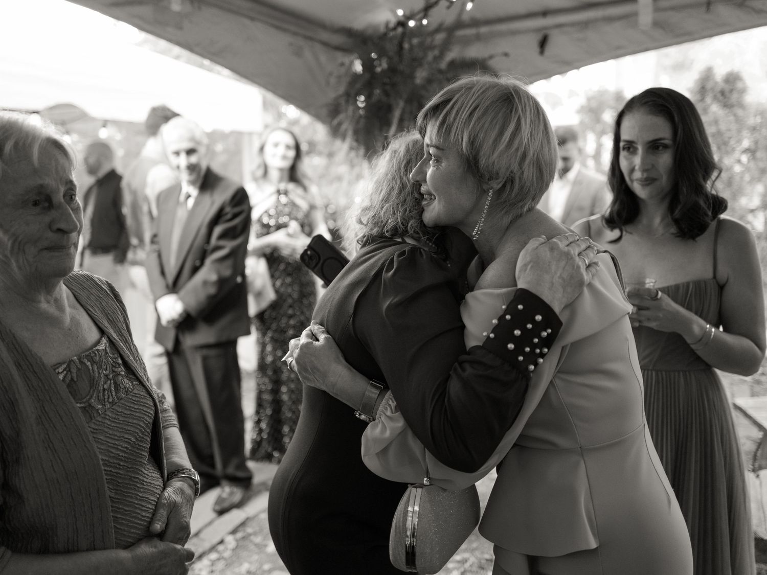 Black and white photos capture wedding reception guests mingling and celebrating under a tent.