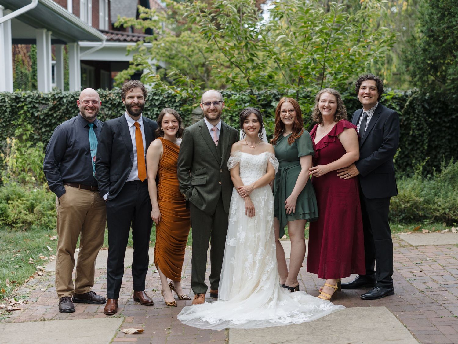 A group poses together on brick pavers for formal event photos in a garden setting.