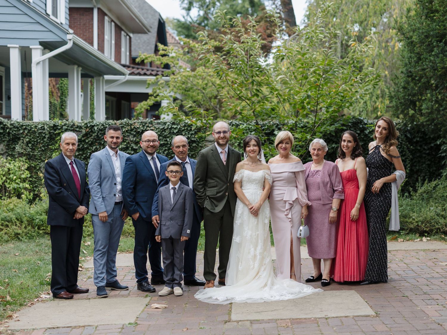 Wedding party group photo outdoors with bridesmaids in pink dresses gathered on residential porch steps.
