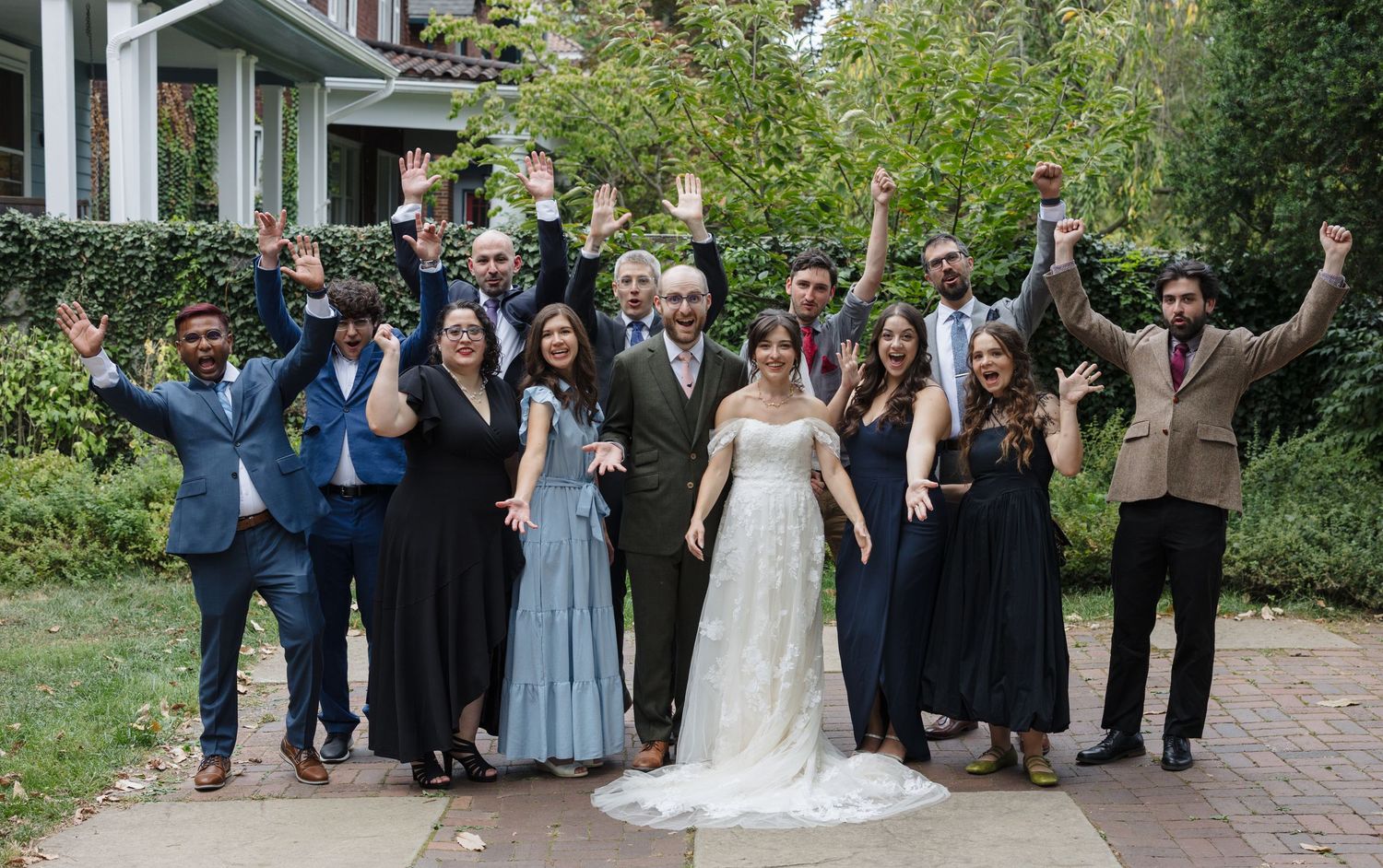 Wedding party celebrating outdoors in front of a house with joyful expressions and raised arms.