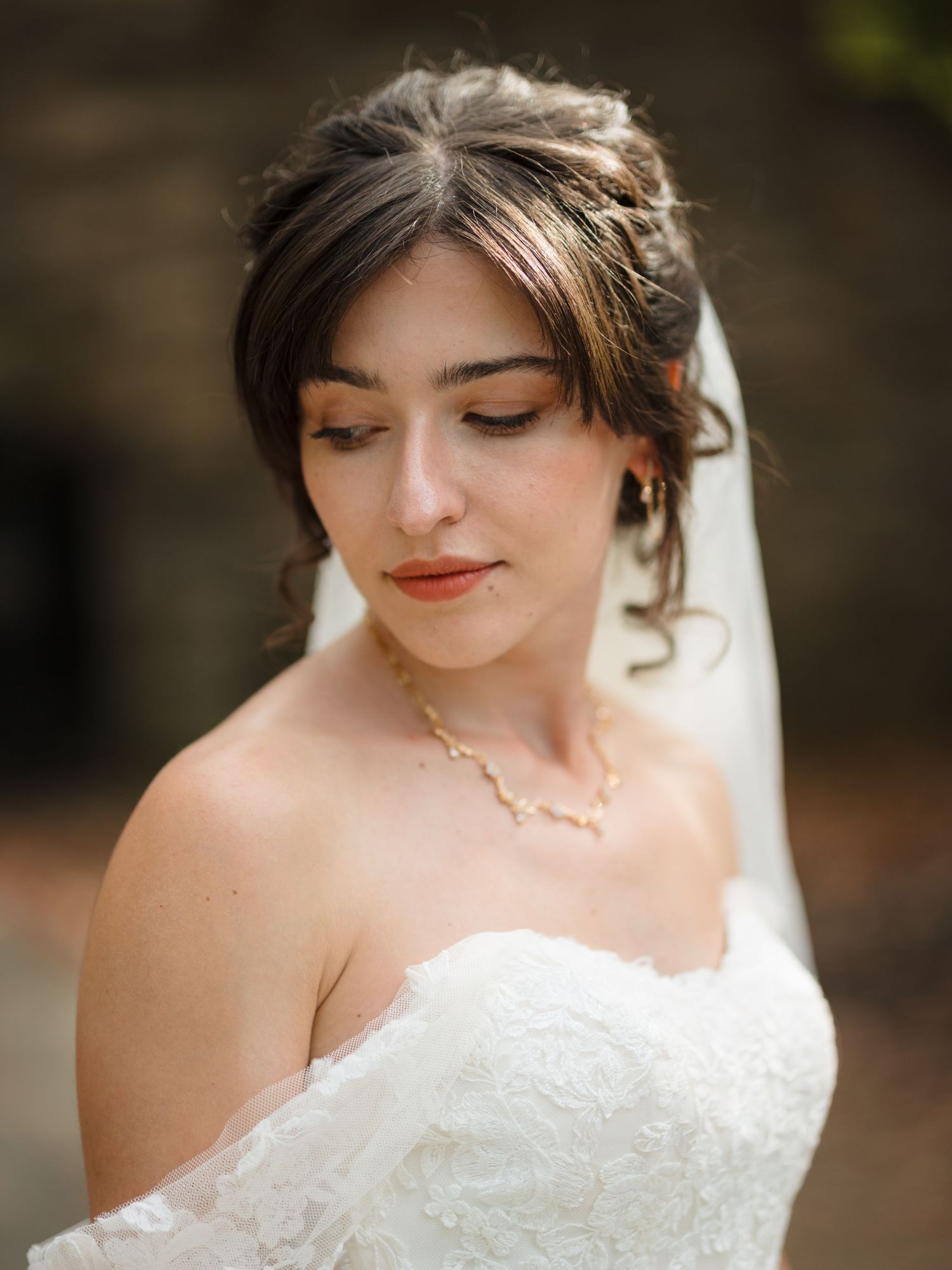 A bride in a white wedding dress with delicate lace details and soft makeup looks down with closed eyes.