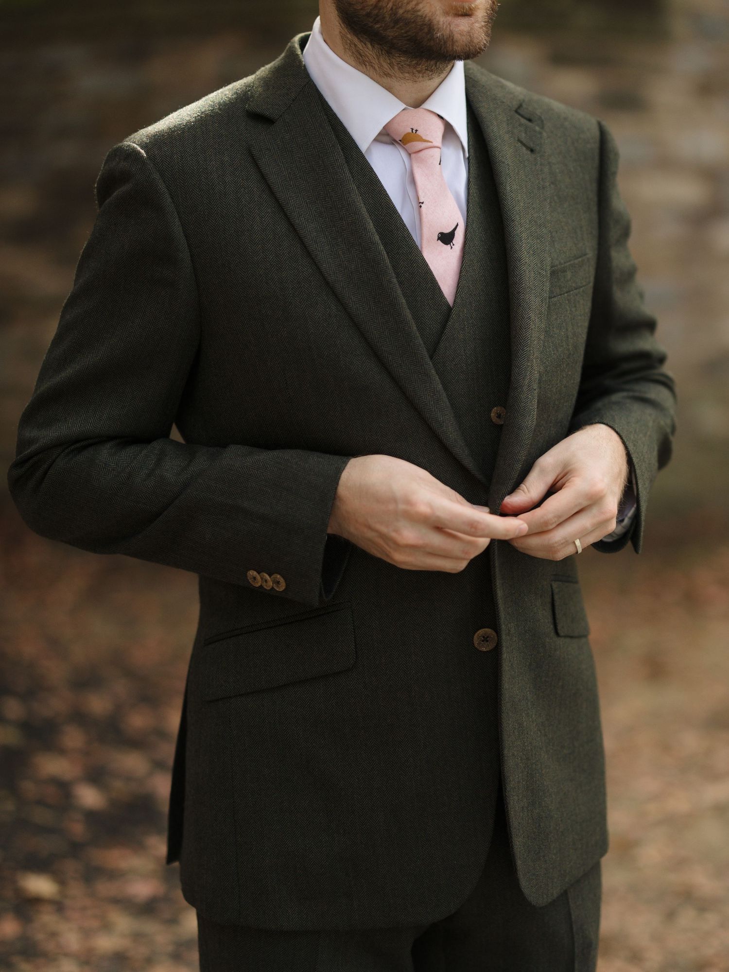A person wearing a dark olive green suit jacket adjusts their attire while standing outdoors.