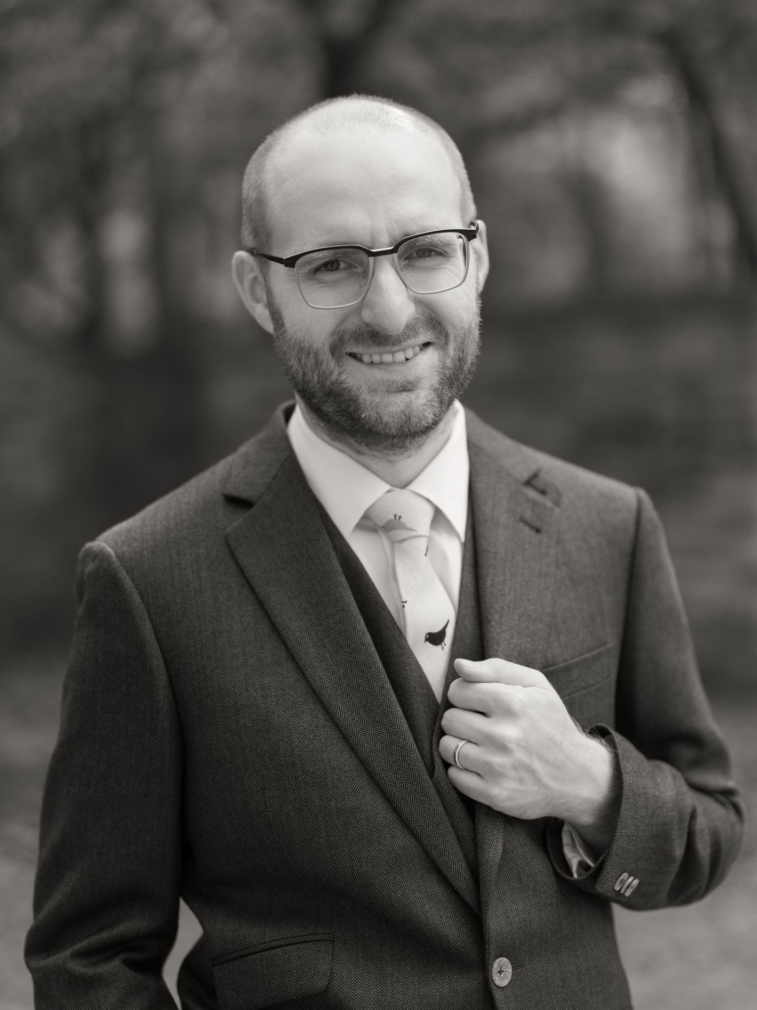 Professional black and white portrait series showing a smiling man in glasses and suit adjusting his tie.