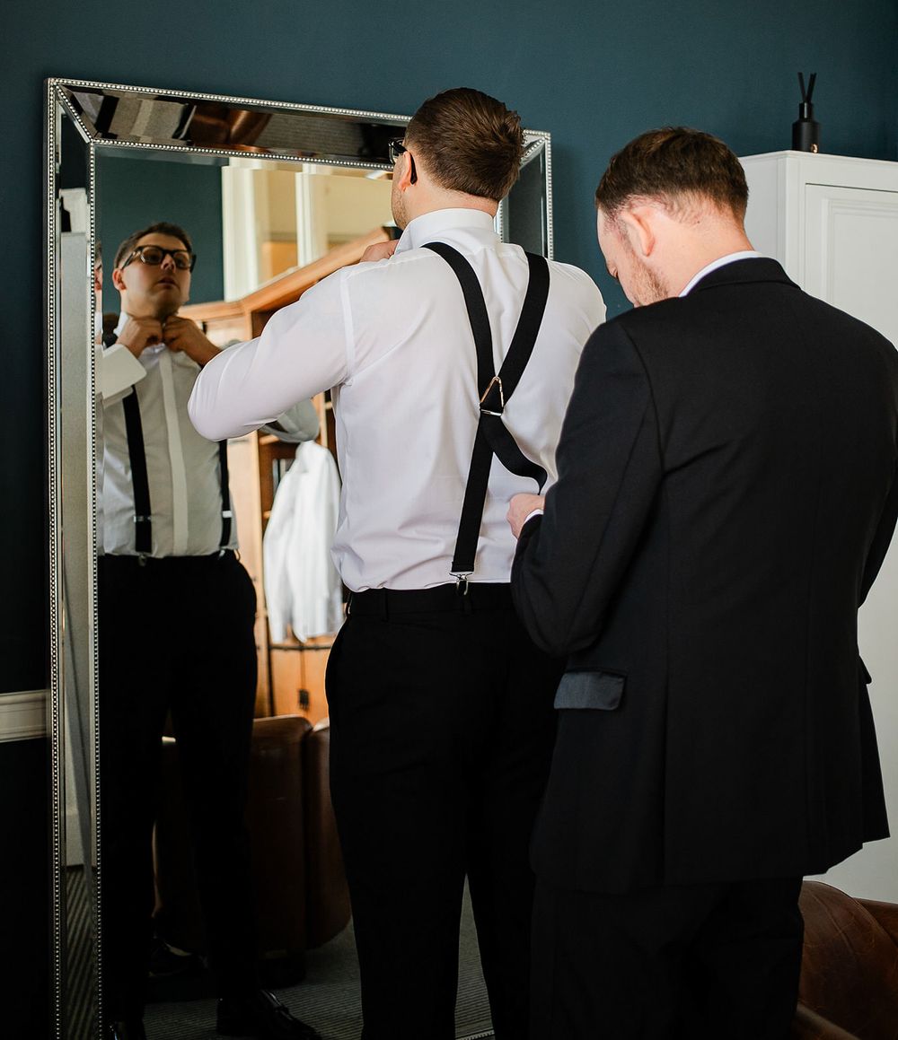 A group of formally dressed people stand in a line near a doorway during what appears to be a wedding event.