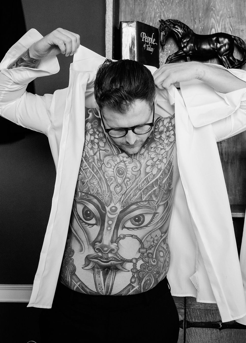 Black and white photo series showing someone lifting their shirt to reveal an intricate owl tattoo design on their torso.