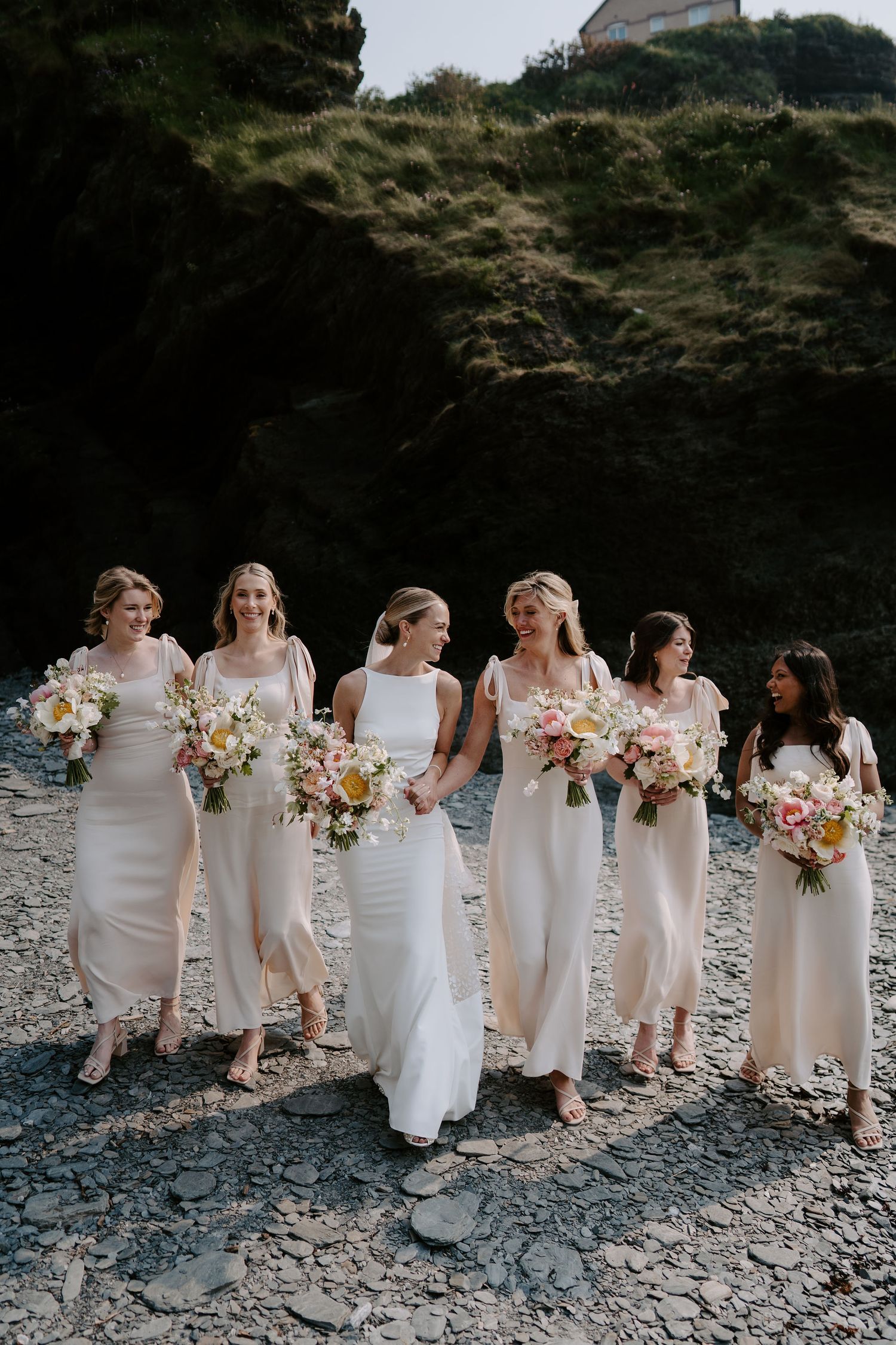 Bride and bridesmaids walking on beach at Tunnels Beach Wedding Venue in North Devon
