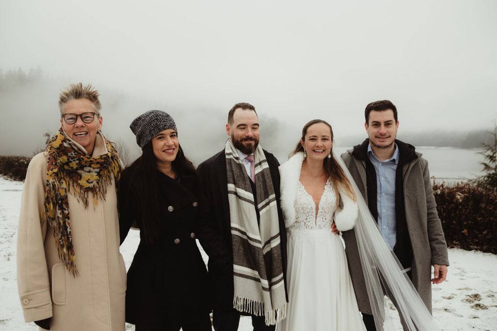 Wedding party of five people posing together in snowy winter setting.