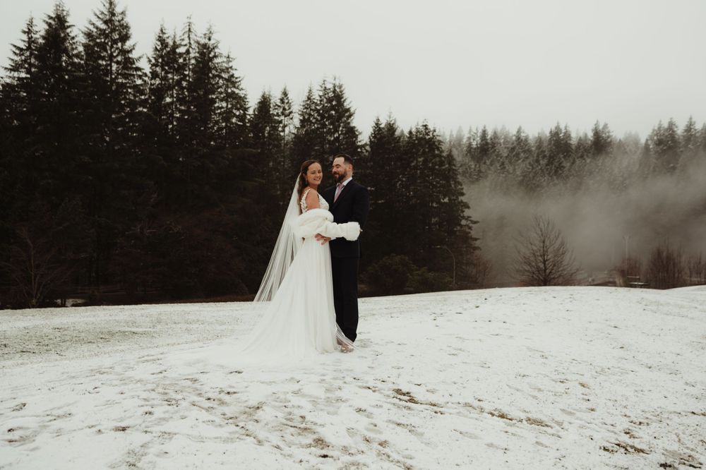Atmospheric wedding portrait in a snowy forest setting with fog rolling through pine trees.