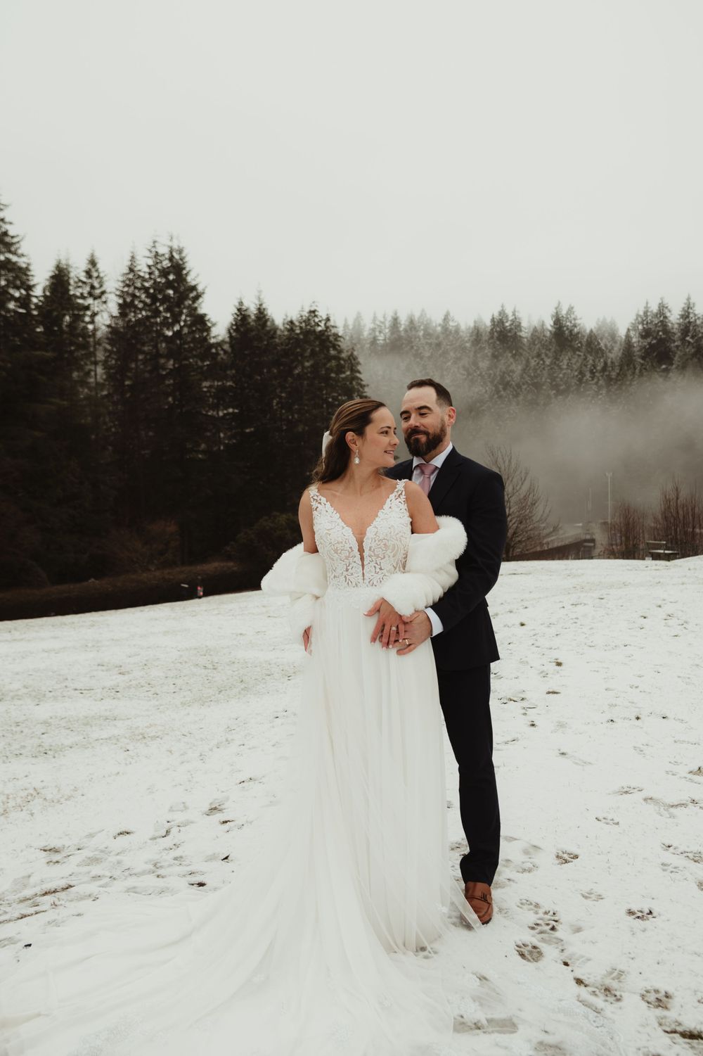 Intimate winter wedding moment with couple embracing in snowy forest setting.