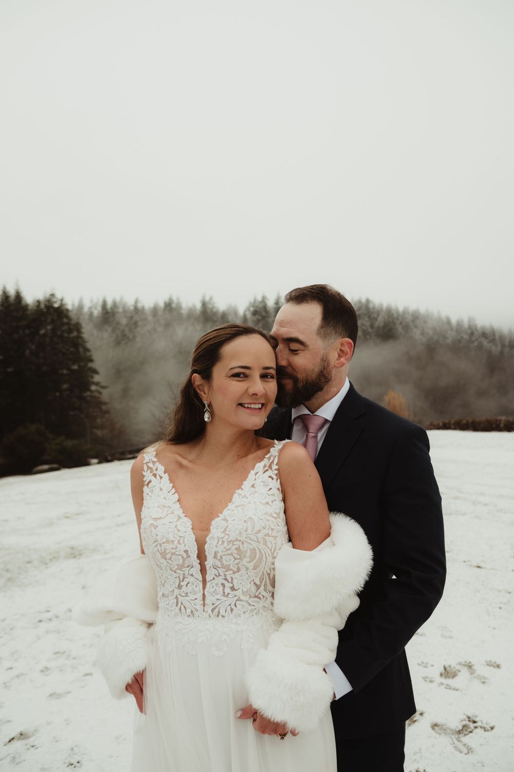 Winter wedding portrait in snow with bride in lace gown and white fur wrap.