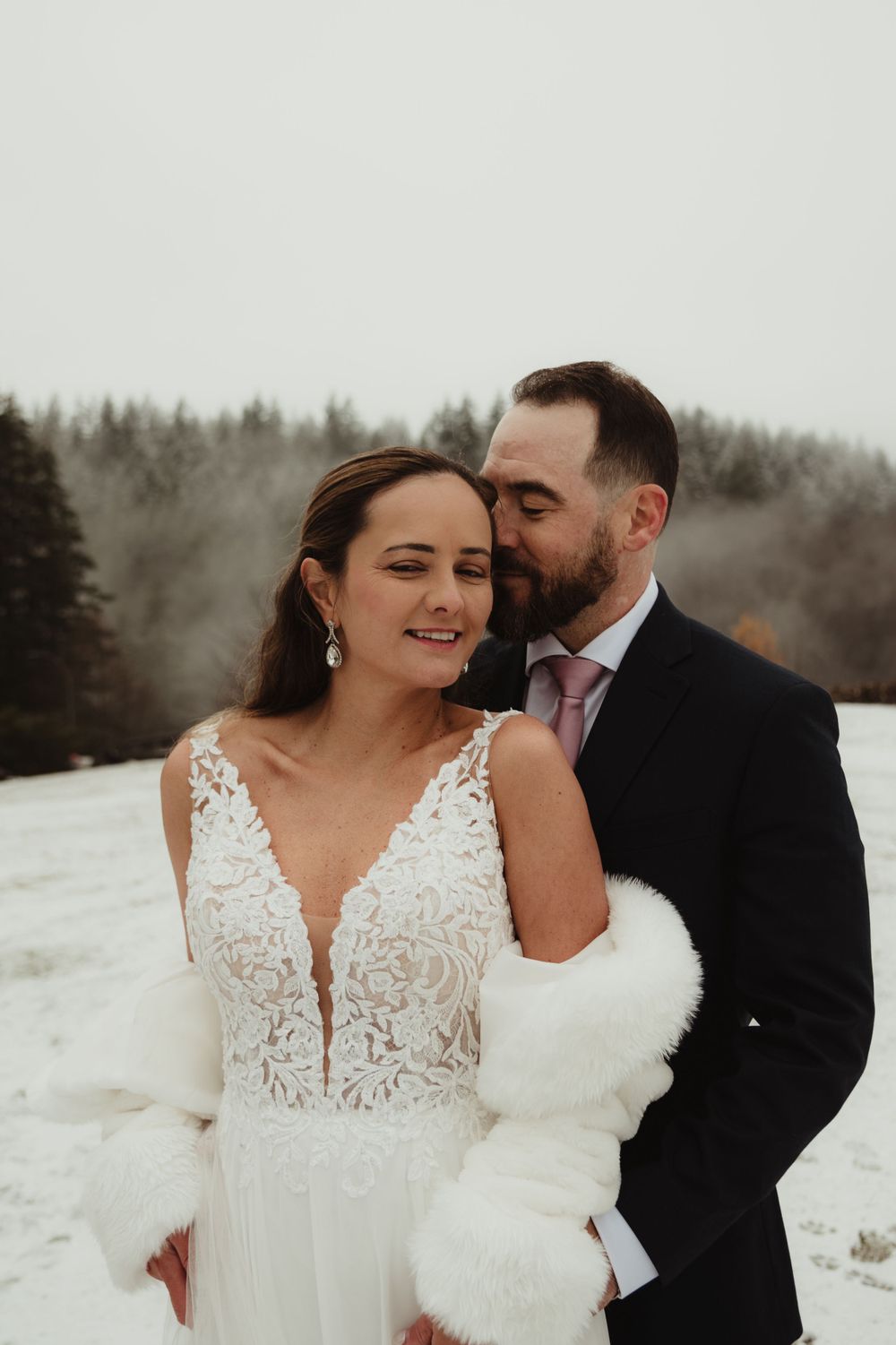 Intimate winter wedding photo with snowy evergreen forest backdrop.