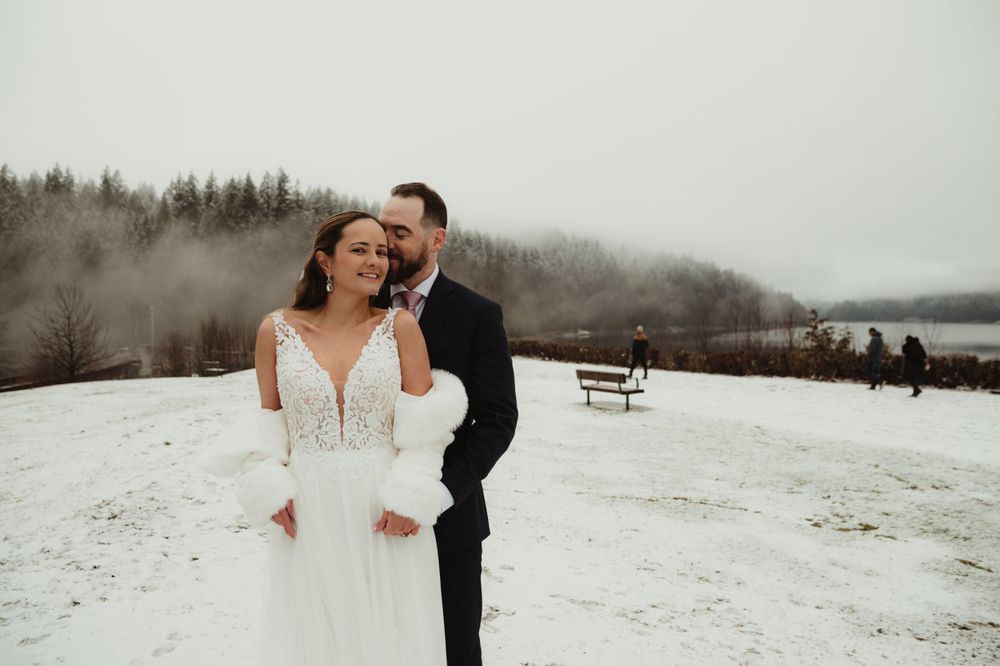 Romantic winter wedding couple embracing in snowy mountain landscape.