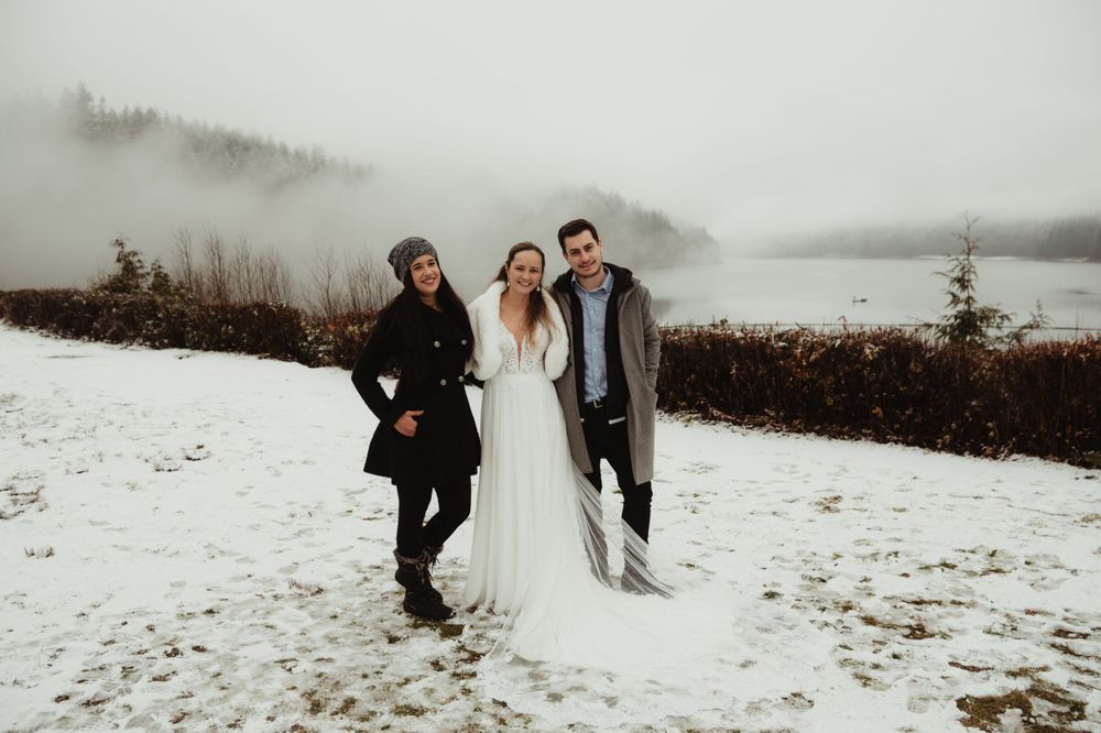 A winter wedding photoshoot near a misty lake with newlyweds and an officiant posing in the snow.