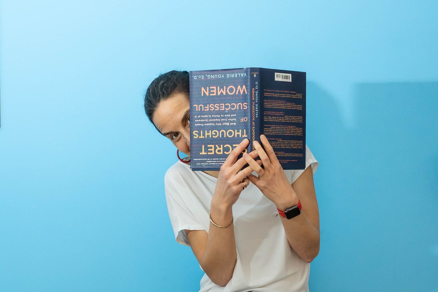 personal branding shoot Brighton of a woman sat in front of a blue walll peeking out from behind a book