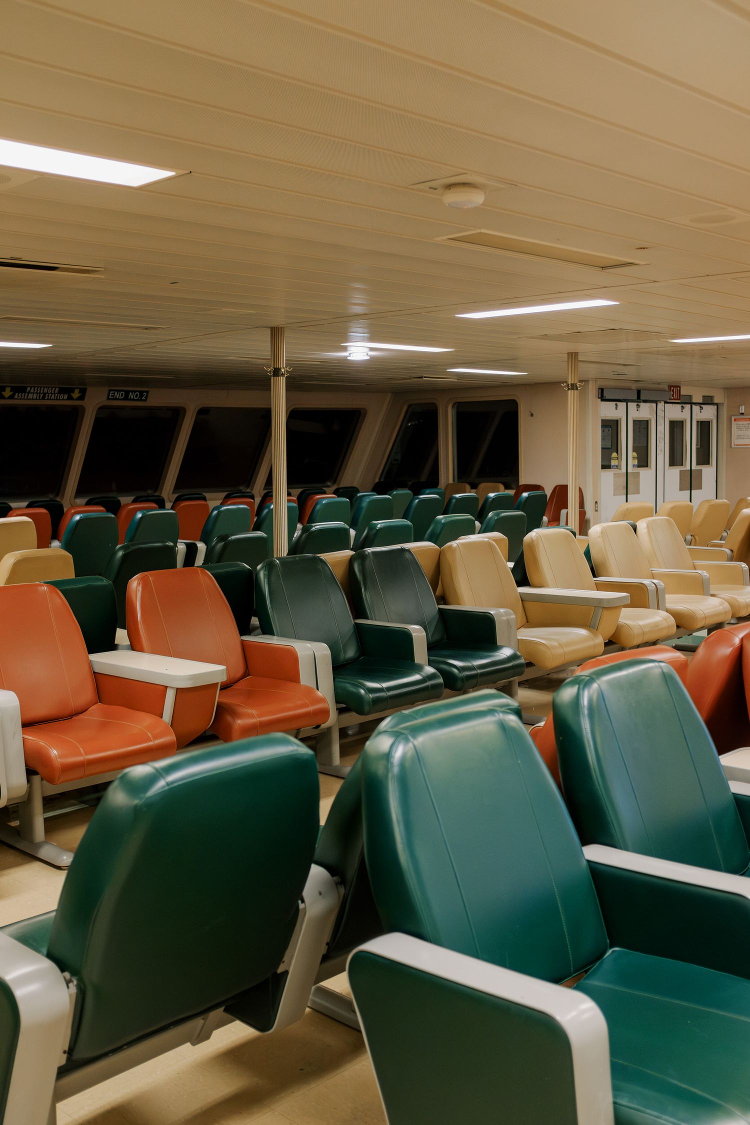 Rows of empty orange, green and beige passenger seats in the interior cabin of a ferry boat.