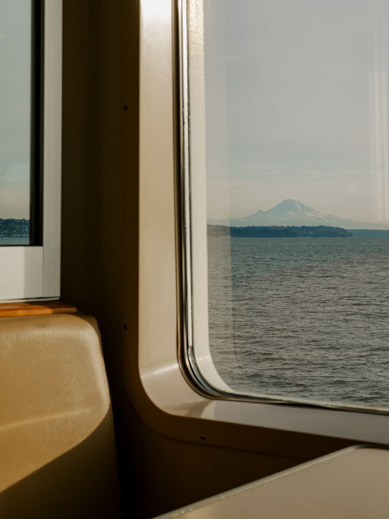 View of a distant mountain seen through a ferry window with tan seats visible in the foreground.