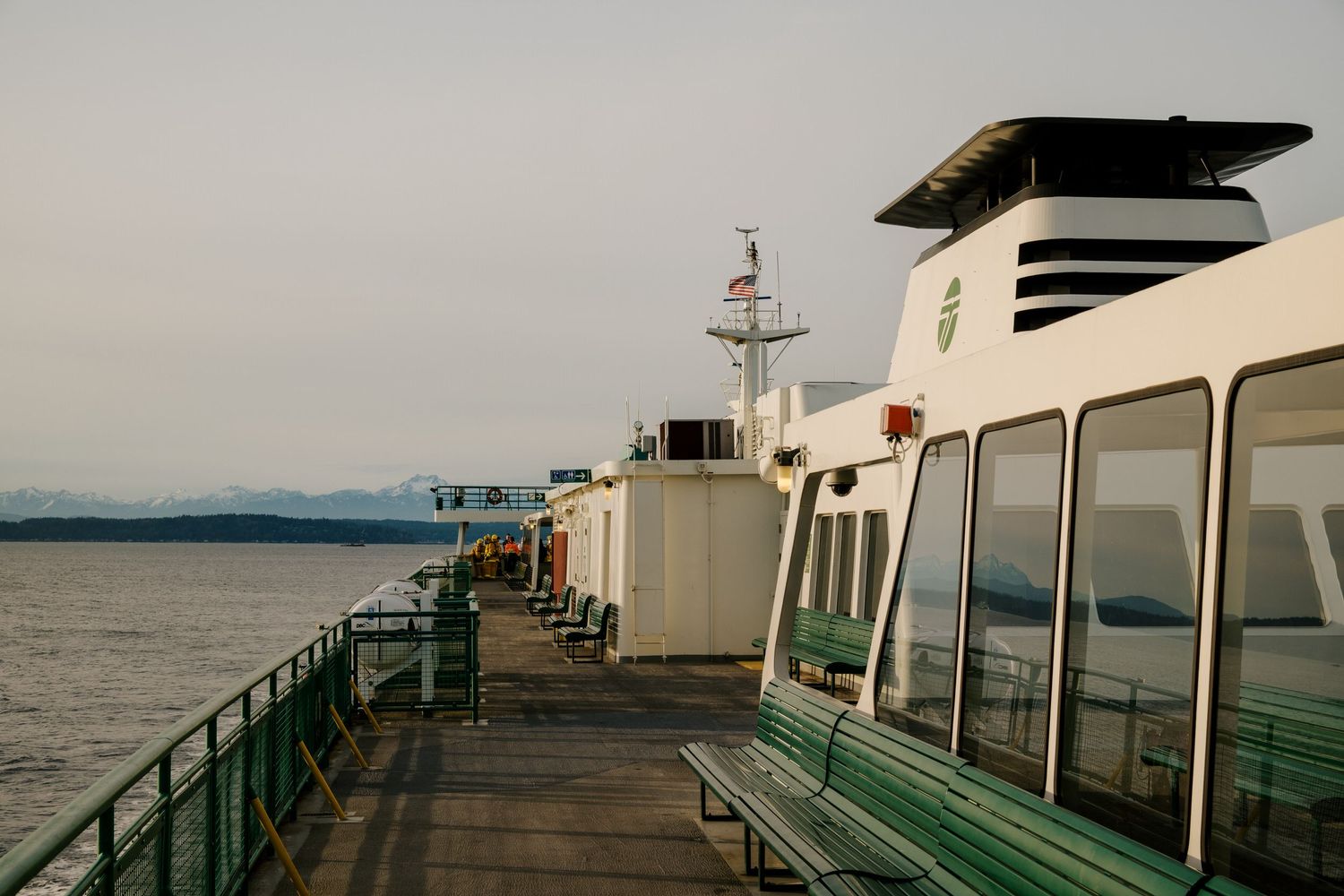 View along the deck of a ferry boat showing white and green passenger cabins against a misty waterfront backdrop.