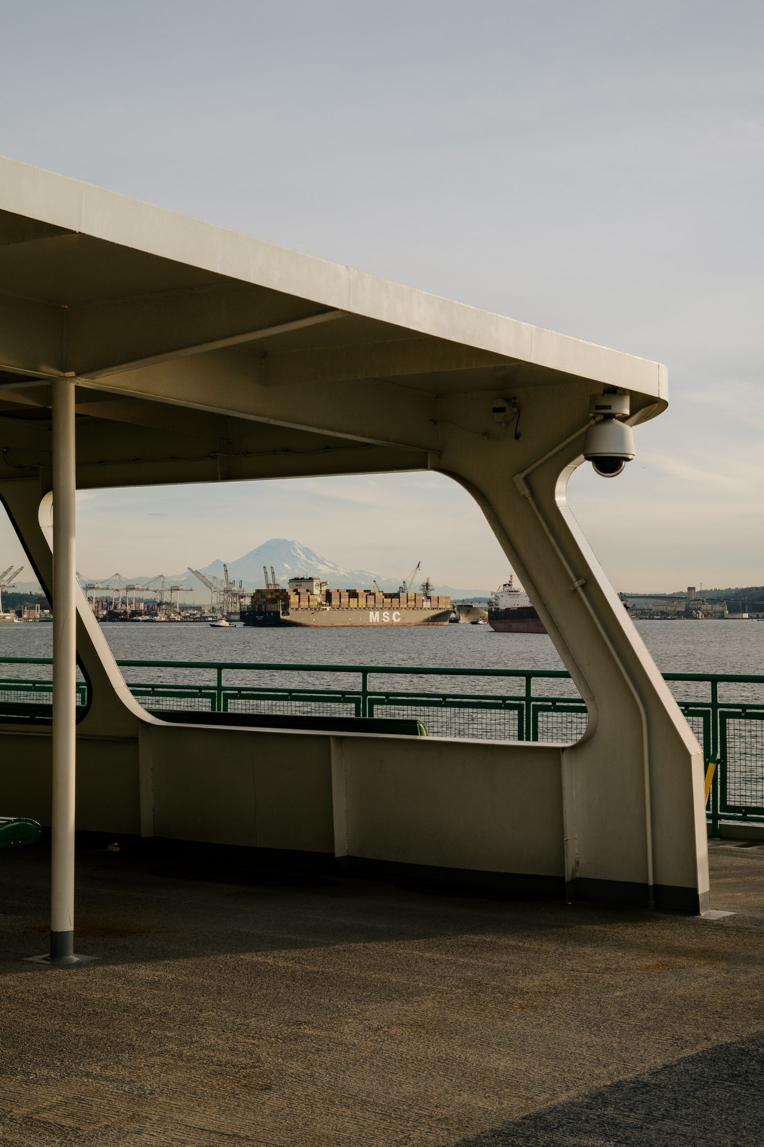 View from a ferry deck showing Mount Rainier and cargo ships in Elliott Bay, Seattle harbor at dusk.