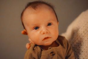 Close up of baby wearing brown sweater with soft lighting.