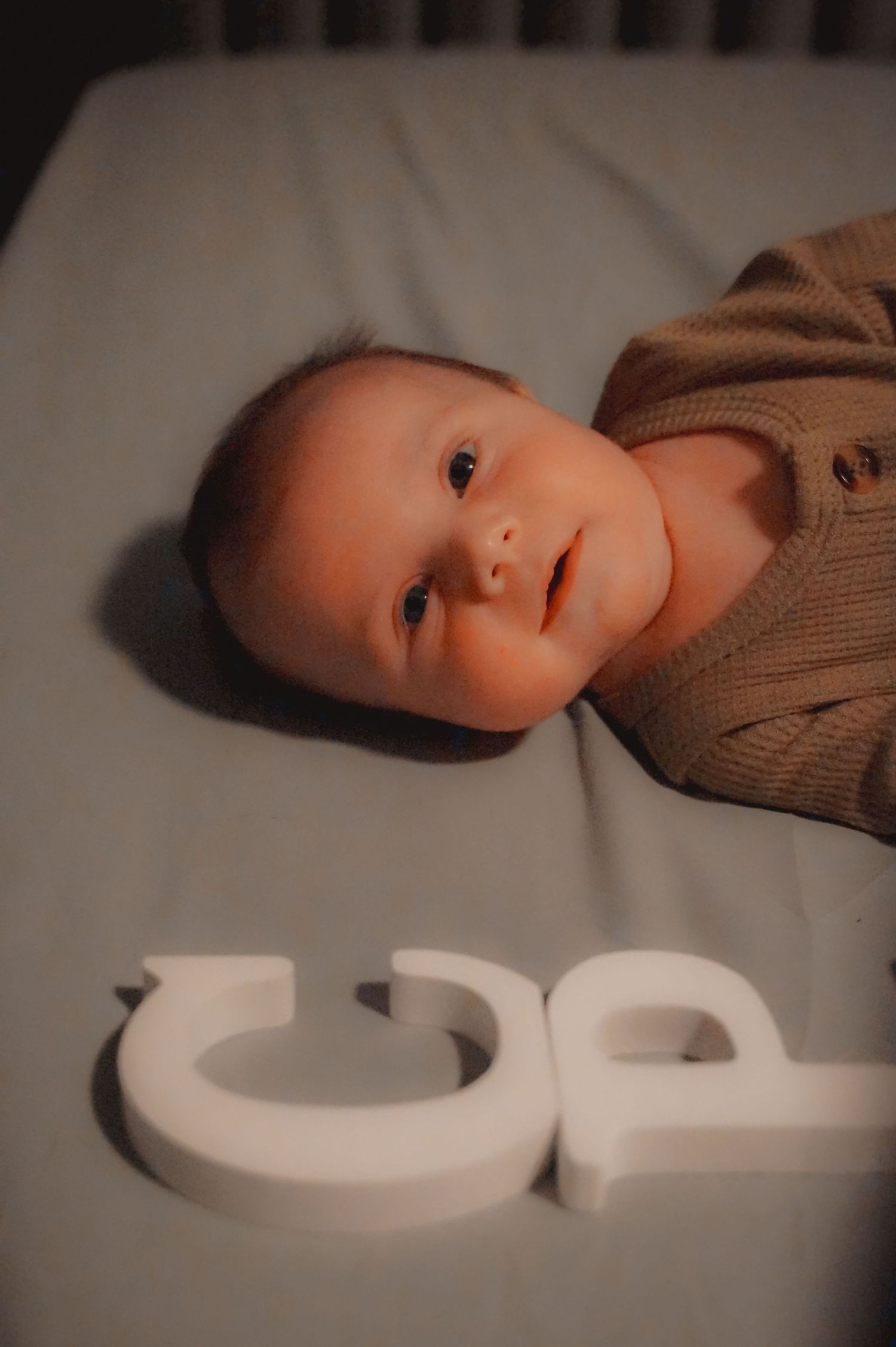 Baby in brown sweater lying next to white decorative letters.