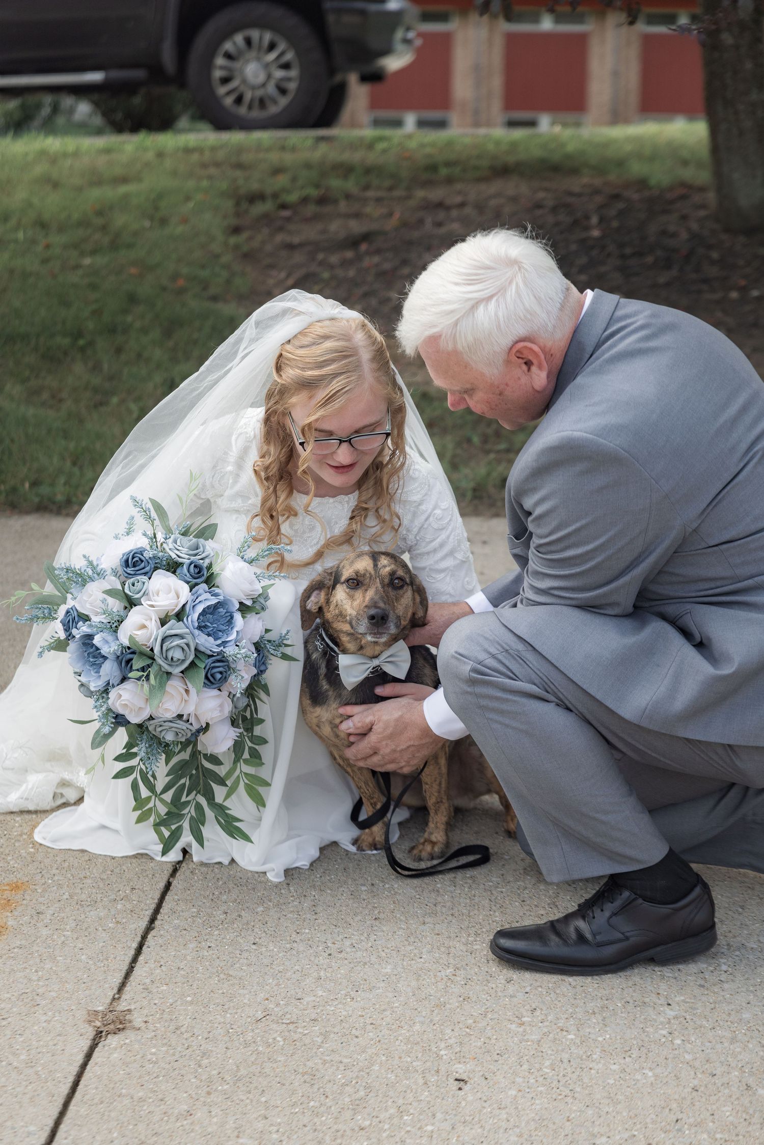 Wedding couple petting a brown dog while holding a blue and white bouquet.