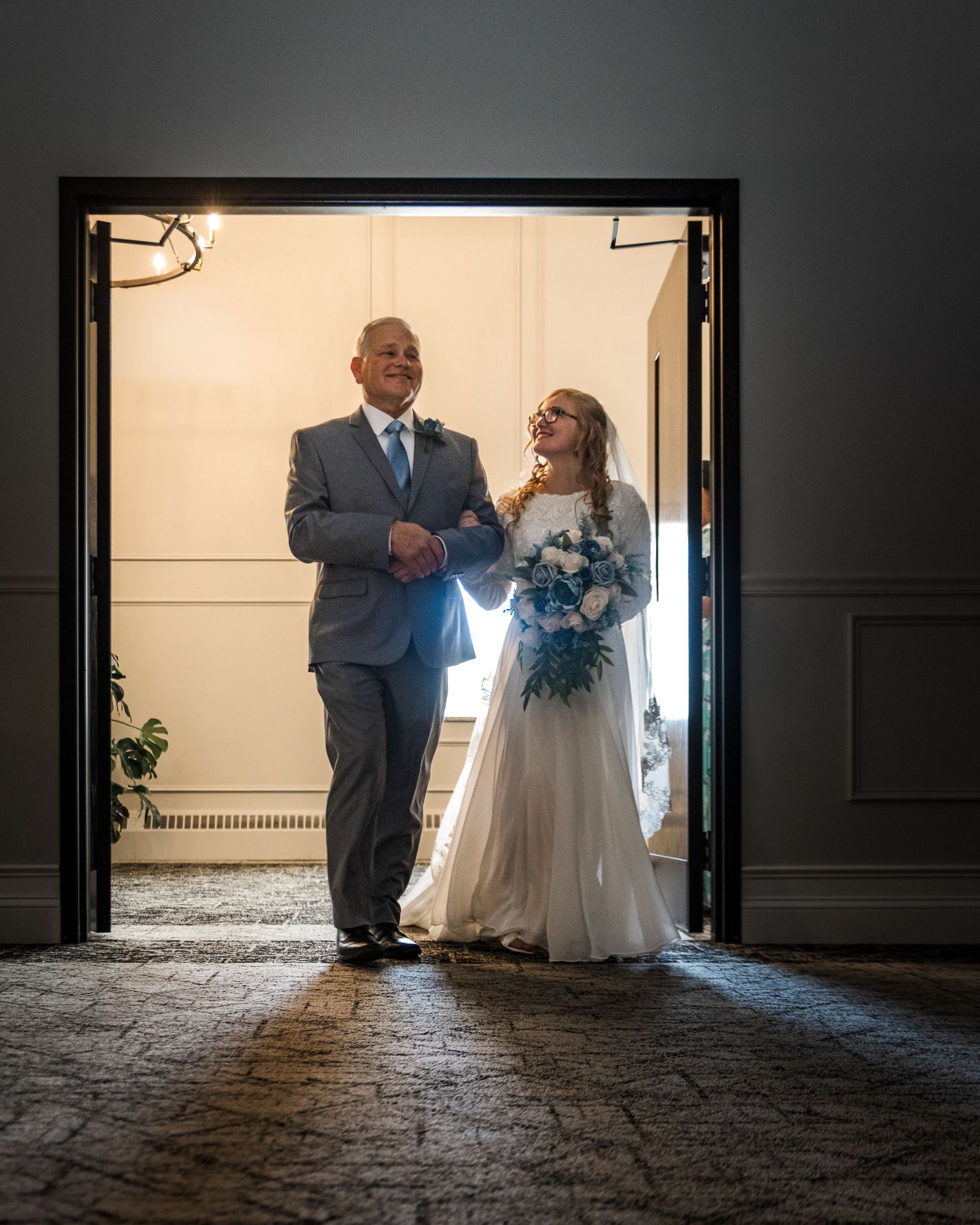 Silhouetted wedding couple entering through dramatic doorway with backlight.