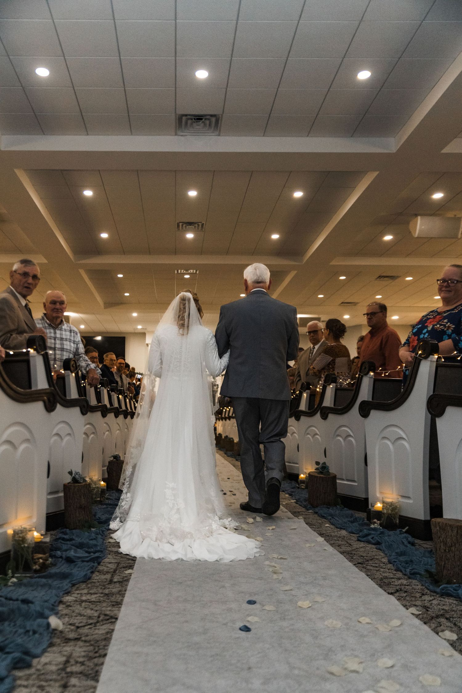 Wedding ceremony procession in elegant ballroom with white chairs and blue carpet.