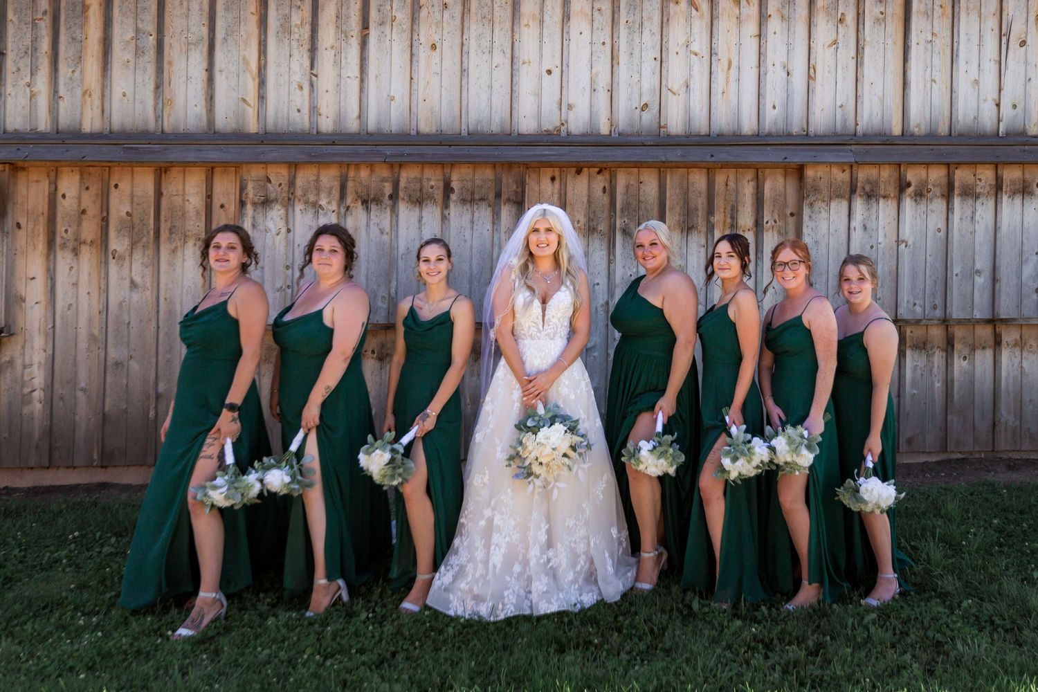 Wedding party seated along rustic wooden fence for casual group photo.